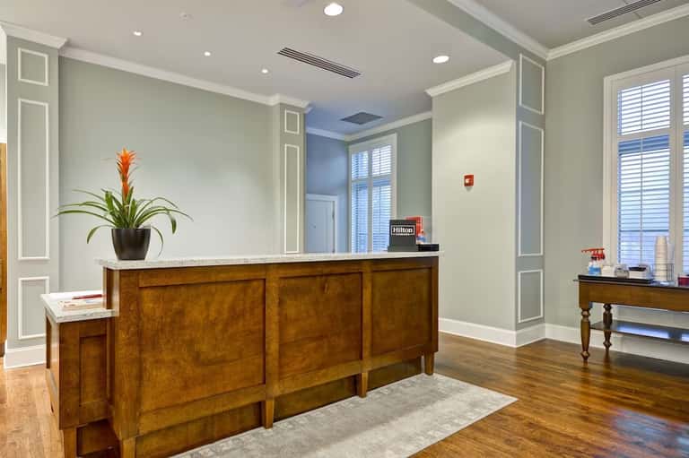 Hotel lobby with wooden reception desk, potted plant, and pale green walls