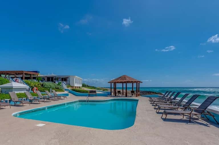 Resort poolside with lounge chairs, gazebo, and ocean view under clear blue sky