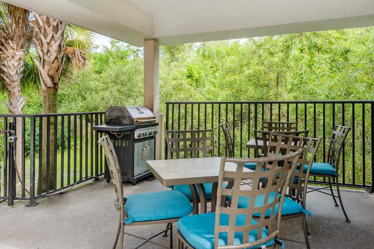 Covered patio with outdoor dining table, gas grill, and chairs overlooking lush green landscape