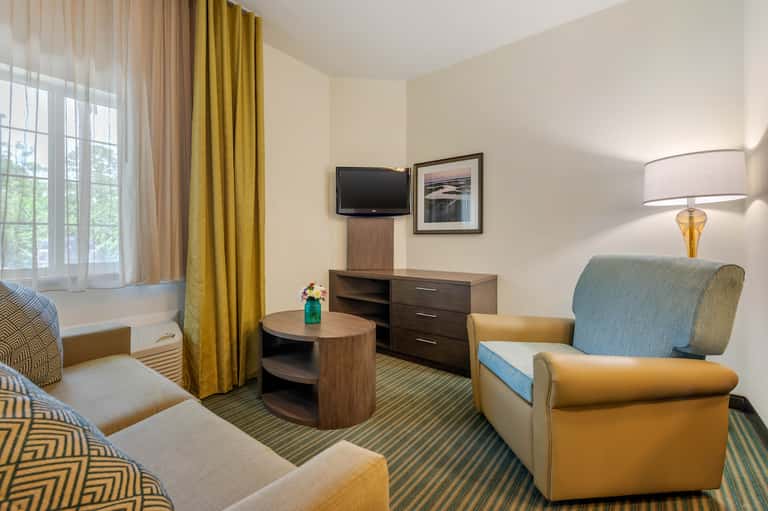 Hotel suite with gold accent chair, TV, wood furniture, yellow curtains, and window seating