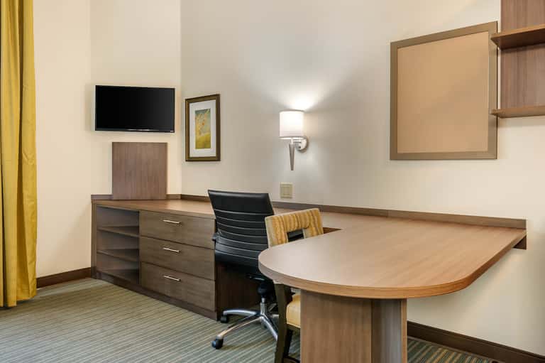 Modern hotel suite with wooden desk, black office chair, TV, and beige workspace décor