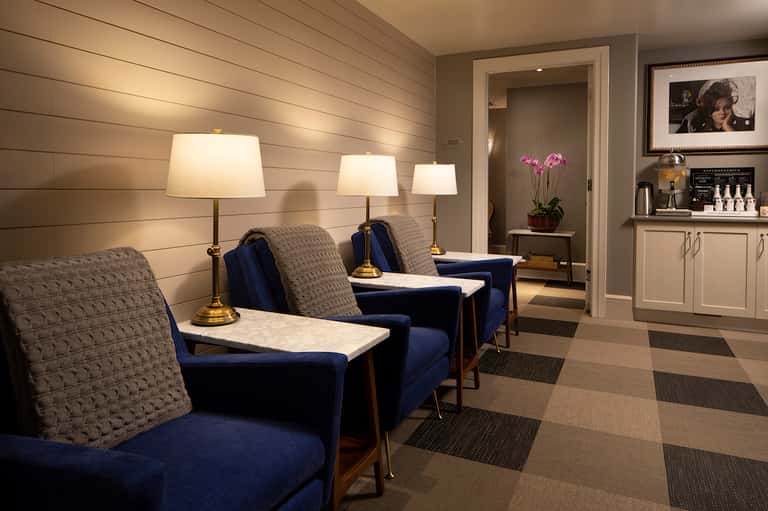 Spa waiting area with blue accent chairs, table lamps, wooden walls, and contemporary furnishings