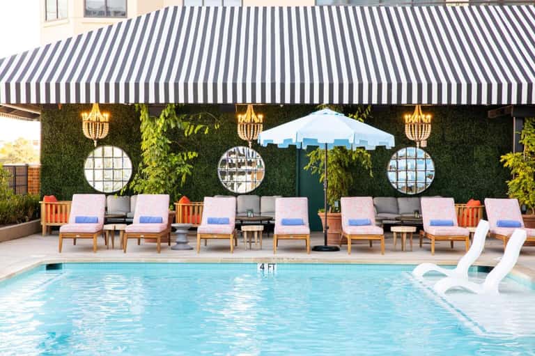 Hotel pool with striped navy awning, wooden lounge chairs, and ivy-covered wall backdrop