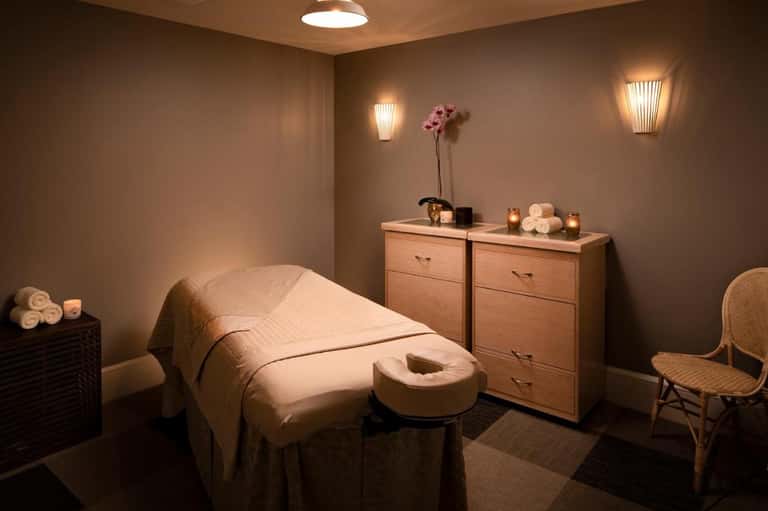 Spa treatment room with massage table, wooden furniture, candles, and warm ambient lighting