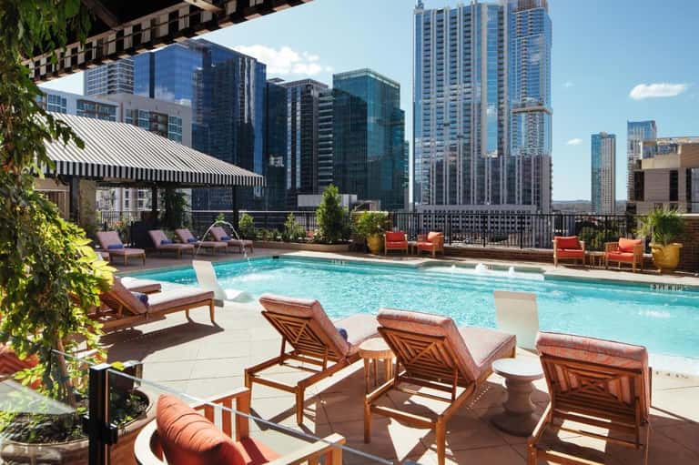 Rooftop pool with wooden lounge chairs overlooking downtown city skyline under clear blue sky