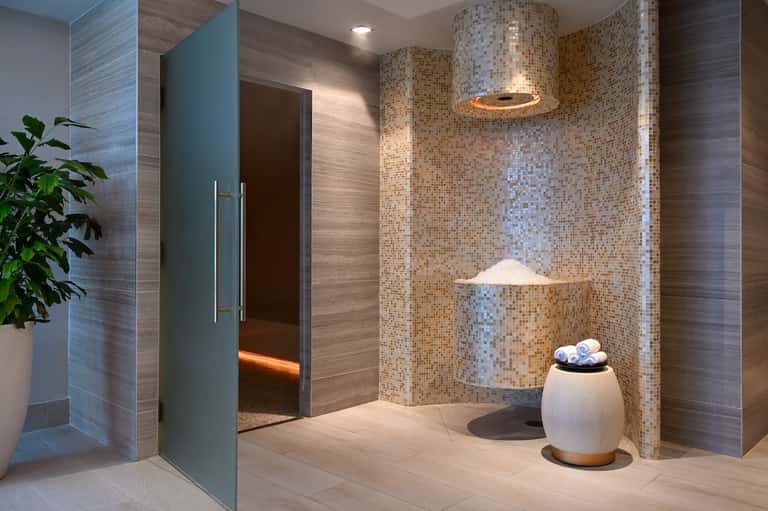 Modern bathroom with rainfall showerhead, mosaic tile walls, neutral tones, and ambient lighting