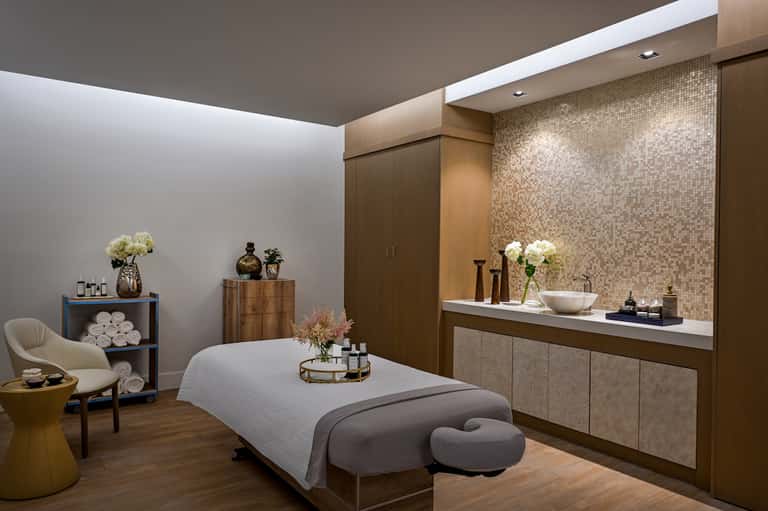 Modern spa treatment room with massage bed, neutral tones, and mosaic tile accents