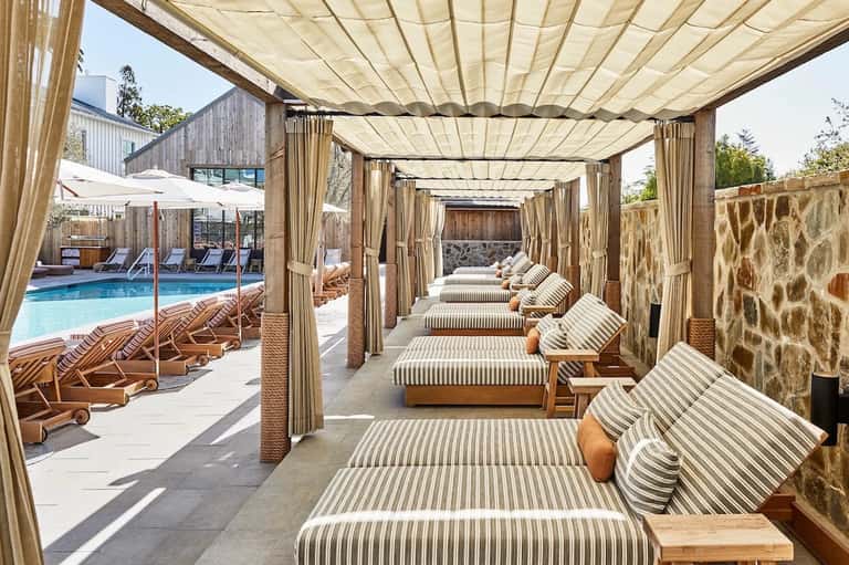 Poolside cabana area with striped loungers under canvas canopy and stone walls