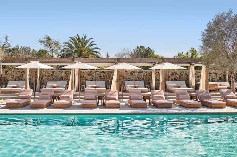 Resort pool with pink loungers and white umbrellas lined up alongside crystal-clear water