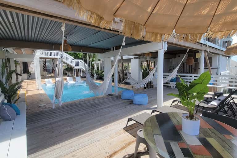 Tropical resort pool area with thatched umbrellas, white pergolas, and hammocks