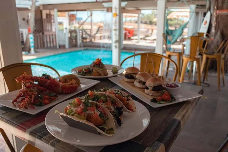 Pool-view dining area with tacos, burgers, and seafood dishes on table overlooking indoor pool