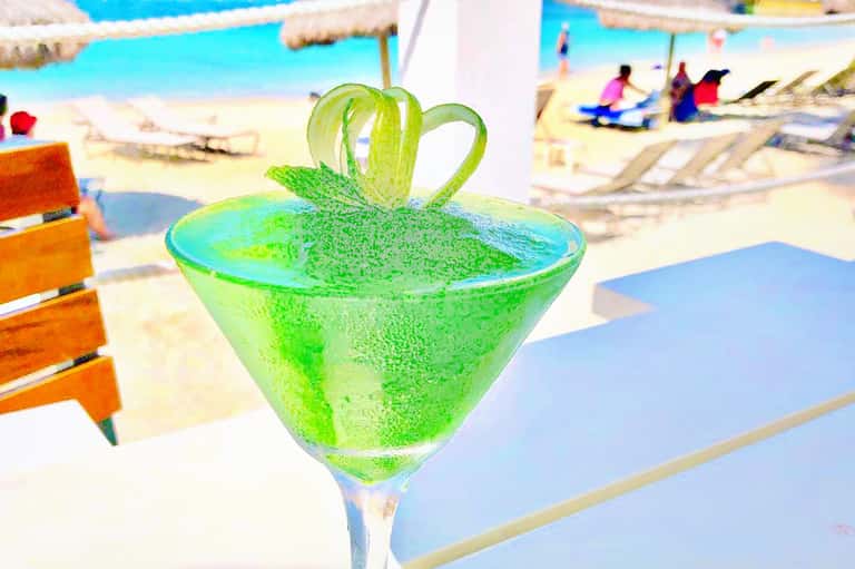 Bright green cocktail with heart-shaped garnish by pool at beach resort with lounging guests