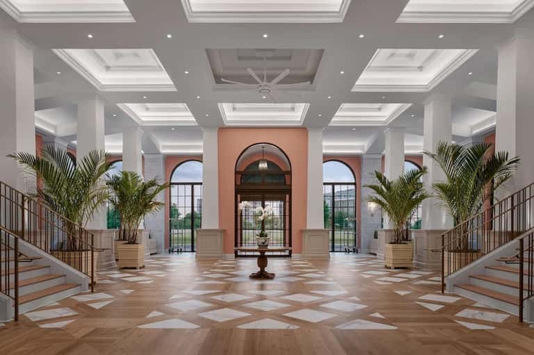 Elegant entrance hall with skylights, palm plants, marble floors, arched doorway, and dual staircases