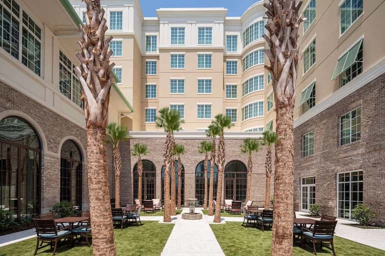 Courtyard with manicured lawn, tall palm trees, surrounding brick buildings, and seating areas