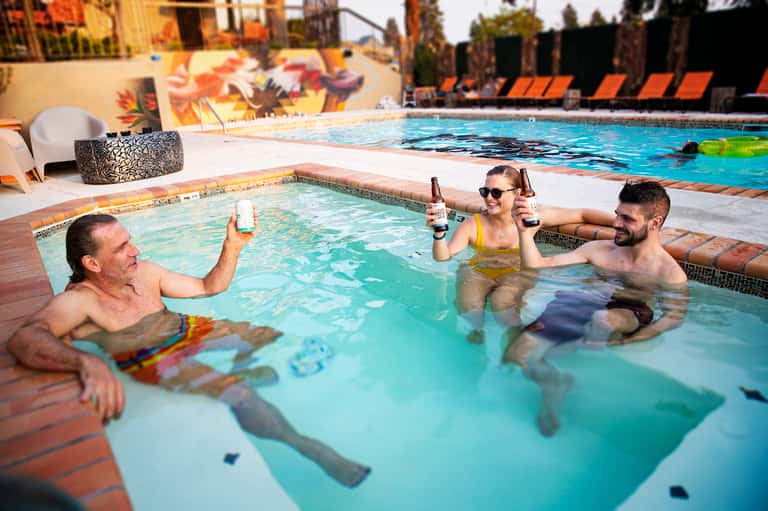 Three guests enjoying drinks in a shallow pool at a resort with colorful mural backdrop