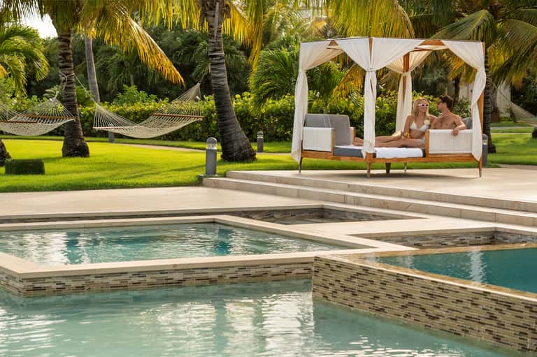 Beachfront resort with canopied daybed, hammocks, multiple pools, palm trees, and ocean view