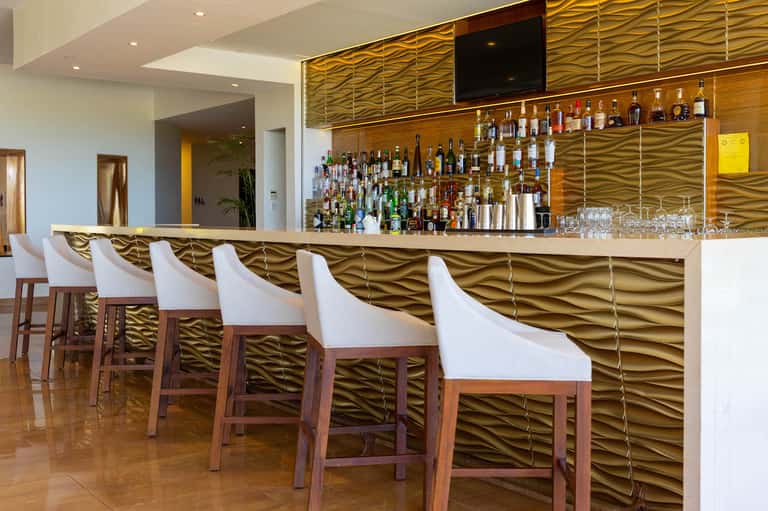 Modern bar with gold wavy wall paneling, white bar stools, and extensive liquor bottle display