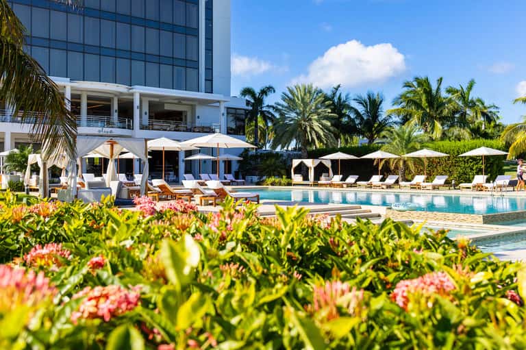 Resort pool area with loungers, umbrellas, and modern hotel building surrounded by tropical landscaping