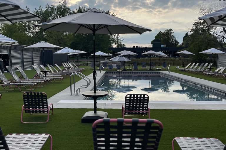 Resort swimming pool surrounded by green lawn, lounge chairs with umbrellas, and changing cabins