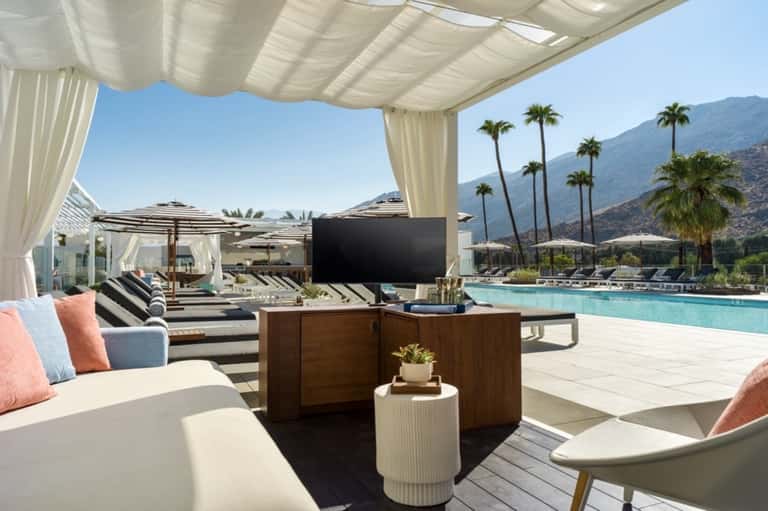 Poolside lounge area with striped sunbeds, white canopy, mountain views, palm trees, and outdoor seating
