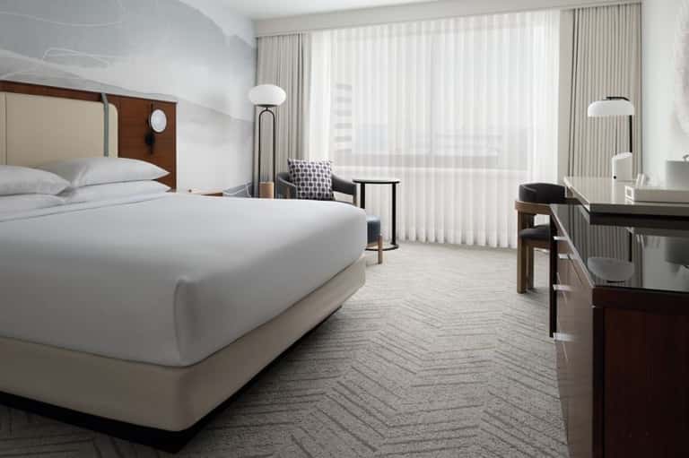 Modern hotel bedroom with king bed, floor-to-ceiling windows, and contemporary furnishings