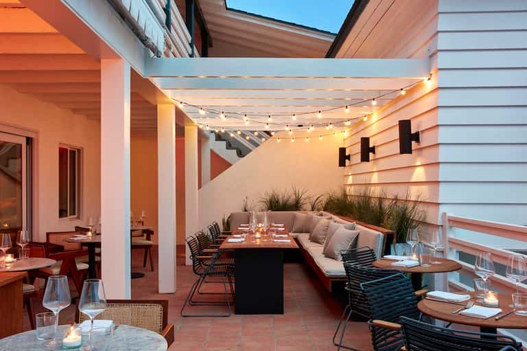 Rooftop dining patio with string lights, built-in seating, white pergola, and city views at dusk