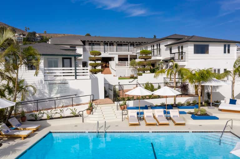 Resort pool area with lounge chairs, umbrellas, and white modern buildings