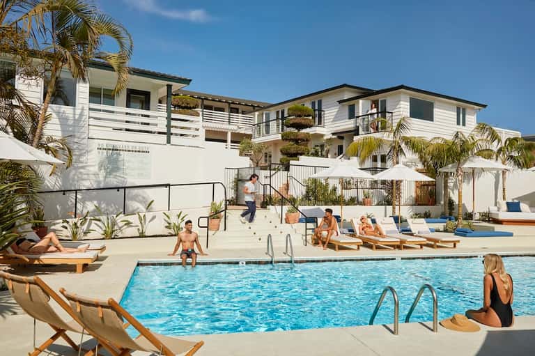 Resort pool area with lounge chairs, palm trees, and white residential buildings in background