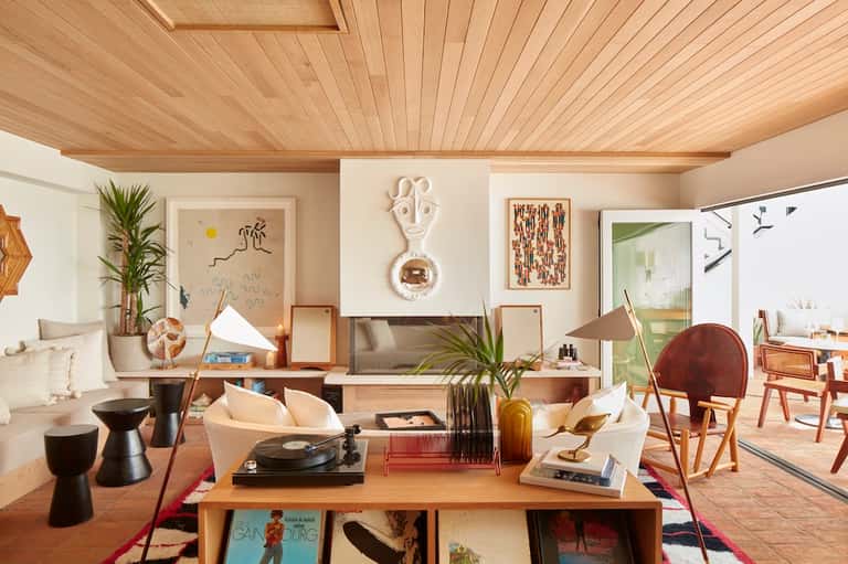 Mid-century modern living room with wood ceiling, blue sofa, plants, wall art, and open floor plan