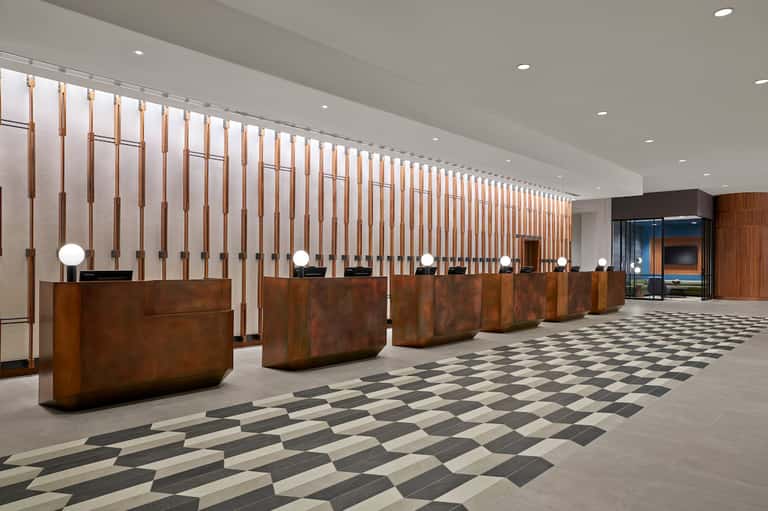 Hotel lobby with multiple wooden reception desks and vertical copper slat wall design