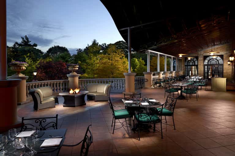 Elegant outdoor terrace with fire pit, dining tables, lounge seating, and manicured gardens at dusk