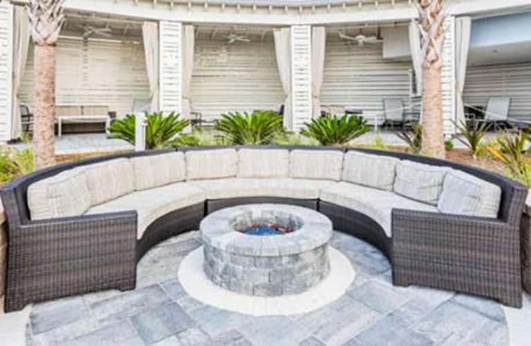Curved outdoor seating area with cushions around fire pit surrounded by white pillars and palm trees