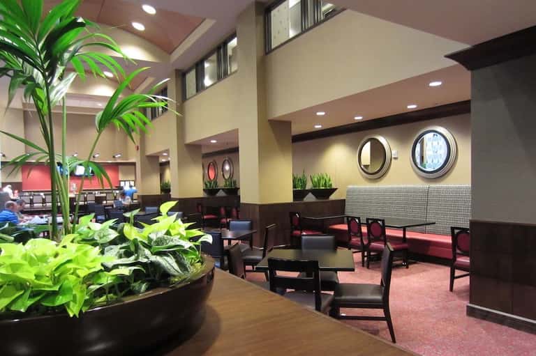 Hotel lobby lounge with high ceilings, potted plants, round mirrors, dark wood furniture, and soft lighting