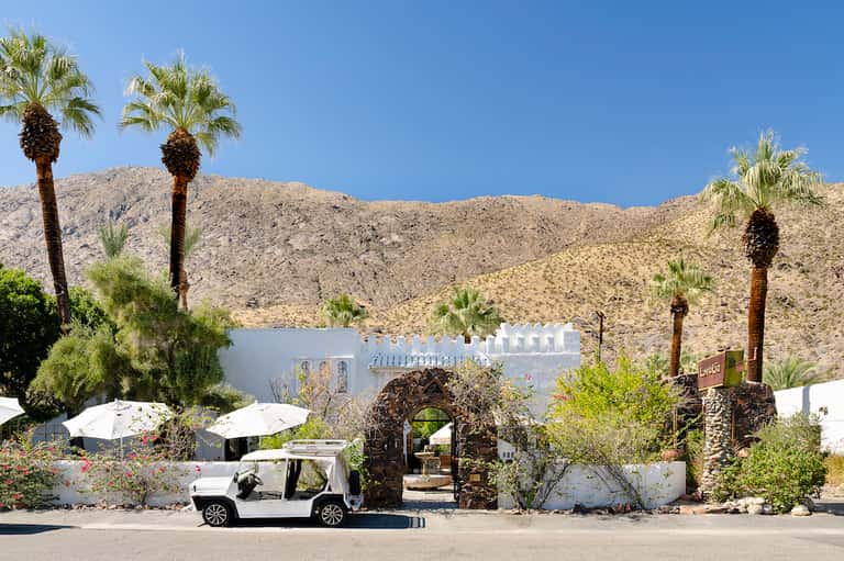 Desert resort entrance with white architecture, palm trees, and mountain backdrop