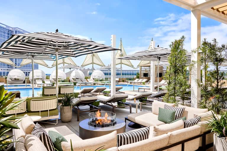 Luxury rooftop pool deck with striped umbrellas, loungers, fire pit, and city skyline views
