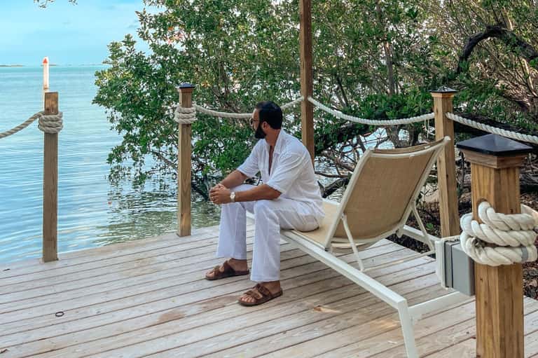 Man relaxing in lounge chair on wooden deck overlooking turquoise water with mangrove trees