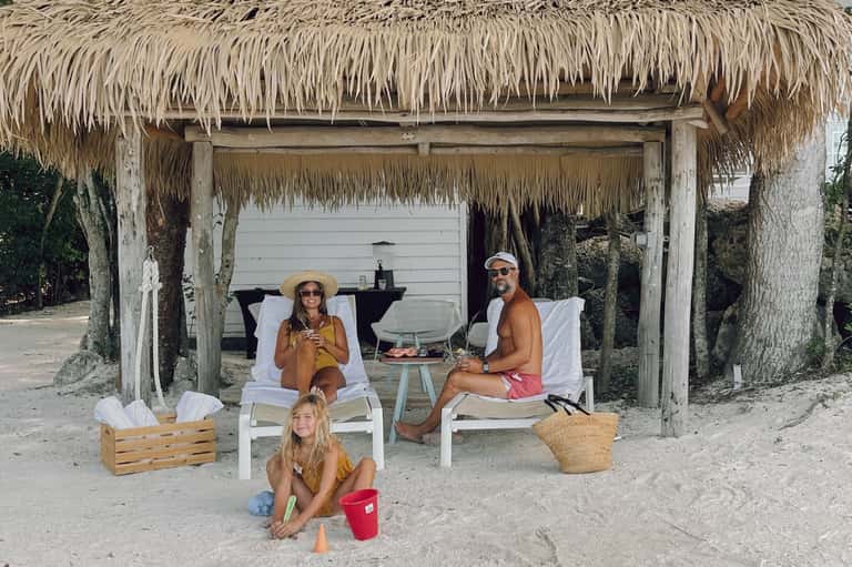 Thatched beach cabana with family relaxing in white lounge chairs overlooking ocean