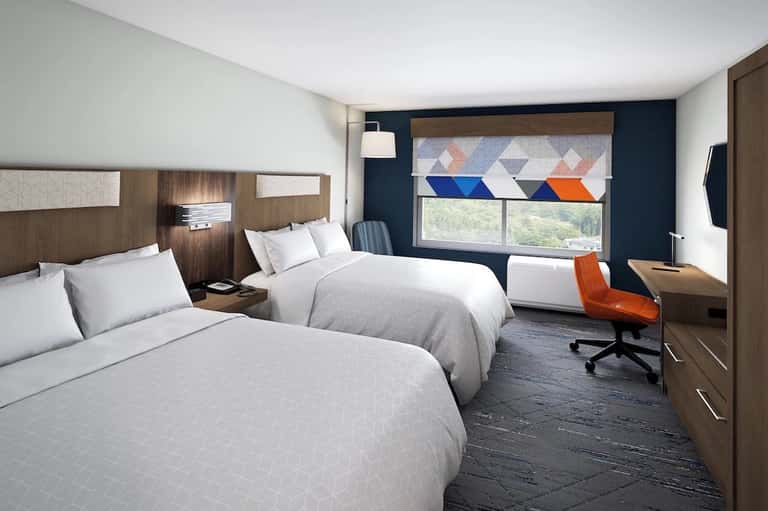 Modern hotel room with two queen beds, dark blue accent wall, and geometric window treatments