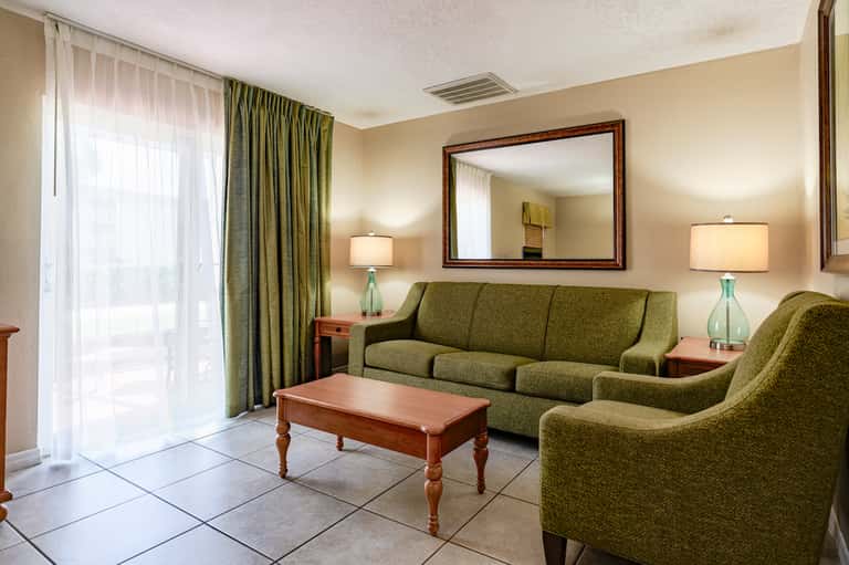 Cozy resort suite living room with green sofa, wooden table, and balcony access