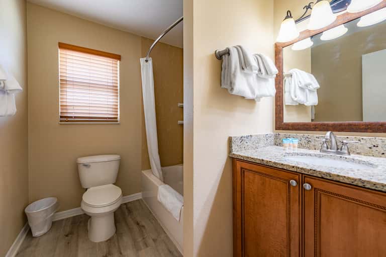 Modern bathroom with granite countertop, wooden vanity, white towels, and tiled shower area