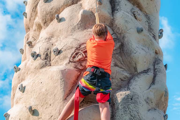 Child rock climbing on indoor artificial climbing wall with holds against blue sky background