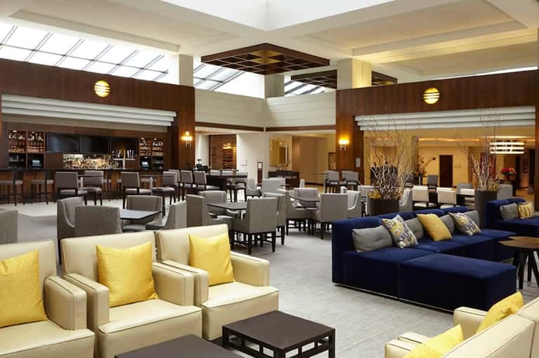 Modern hotel lounge with cream and navy seating, wood accents, and bar area
