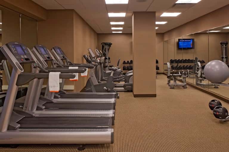 Fitness center with rows of treadmills, exercise bikes, dumbbells, stability balls, and wall-mounted TV