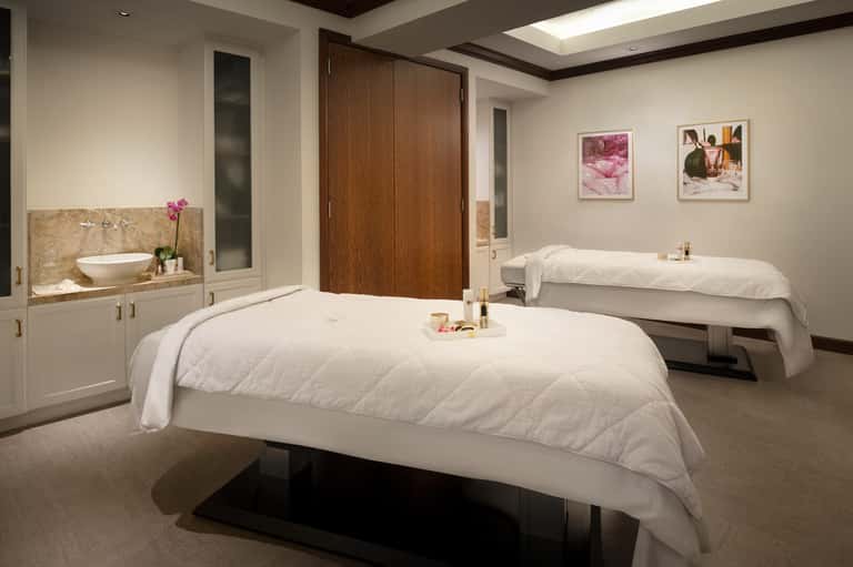 Spa treatment room with two massage beds, sink vanity, and modern neutral décor