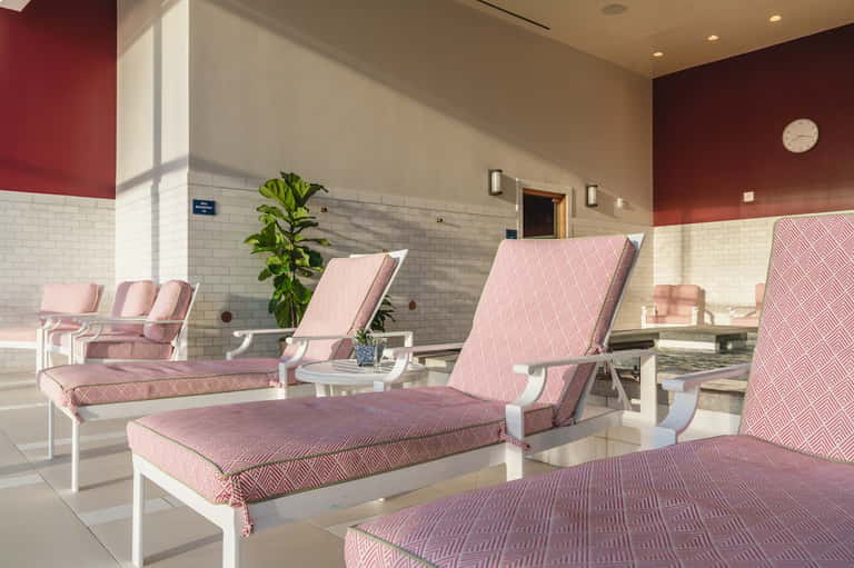 Pink and white lounge chairs arranged in a spa relaxation room with tiled walls