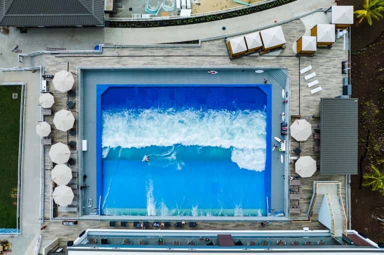Aerial view of resort pool with wave design, white umbrellas, and teak lounge chairs