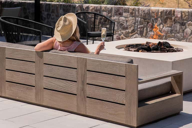 Woman in straw hat relaxing by fire pit with champagne glass and stone wall backdrop