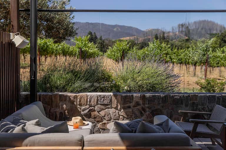 Outdoor lounge with stone wall, comfortable seating, and vineyard views through glass panels