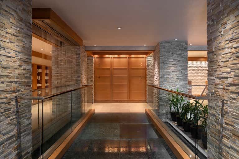 Modern hotel corridor with stone walls, wooden beams, elevator doors, and ambient lighting
