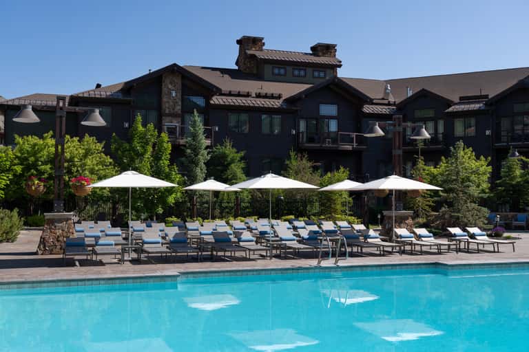 Resort pool with turquoise water, loungers, white umbrellas, and dark lodge-style building
